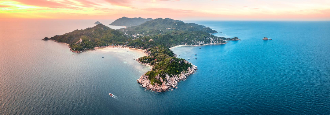 Aerial view of a tropical island surrounded by turquoise-blue ocean waters, featuring lush greenery, sandy shores and a scenic coastal landscape.