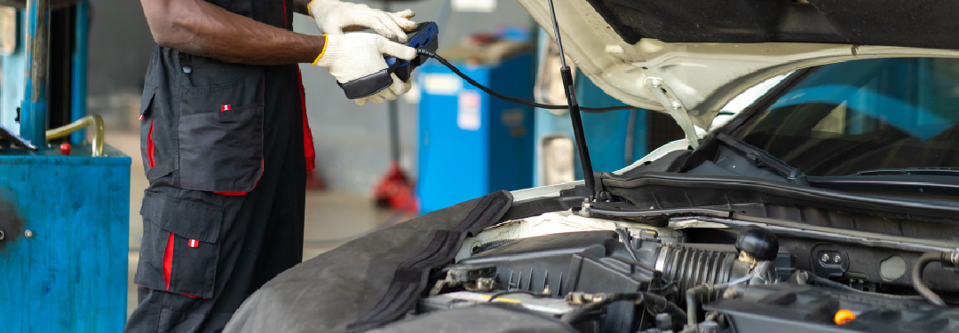 Car mechanic inspecting a vehicle with its bonnet open inside an automobile service workshop.