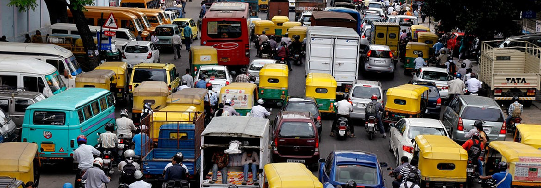 Heavy traffic congestion on a busy Indian city road with cars, auto-rickshaws and motorcycles navigating crowded streets.