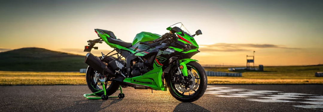 Green Kawasaki Ninja ZX series sport motorcycle parked on a racetrack at sunset, featuring aerodynamic fairings and racing-inspired design.