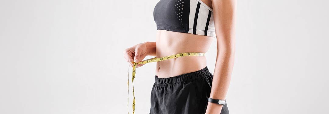 Woman wearing workout clothes measuring her waist with a yellow measuring tape.
