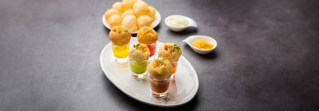 Indian pani puri served in small glasses with colourful flavoured water, topped with crispy puris, sev and fresh herbs.